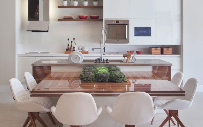 A cozinha com móveis planejados da Evviva Bertolini aproveitou o espaço para fazer uma mesa ligada à bancada que abriga até seis pessoas